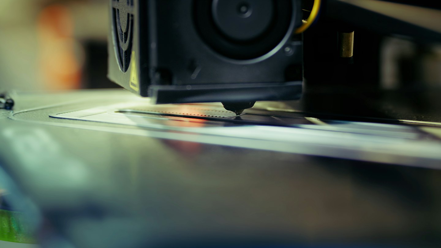 3D printer nozzle extruding plastic onto build plate.