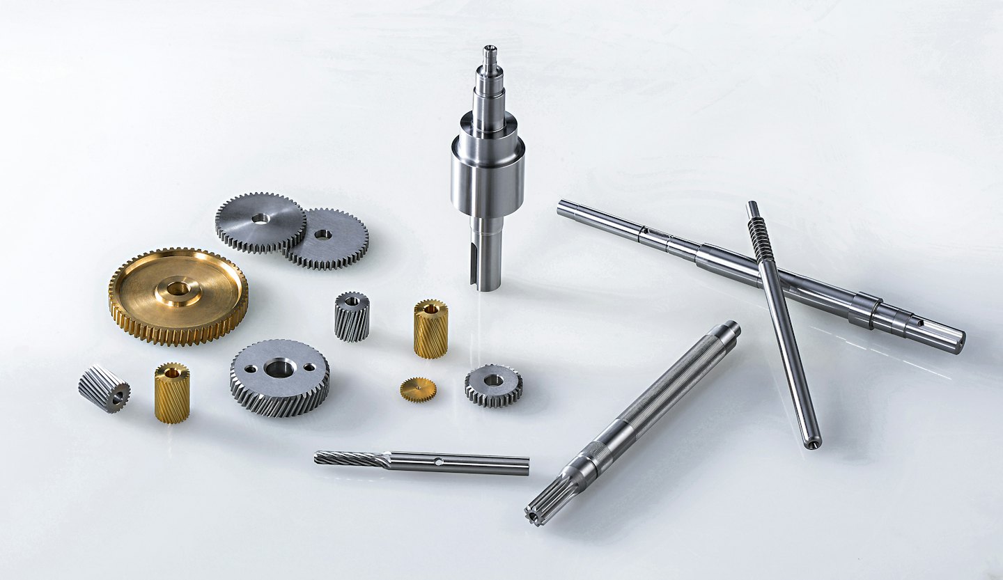 Assorted metal gears and shafts arranged on a white surface.
